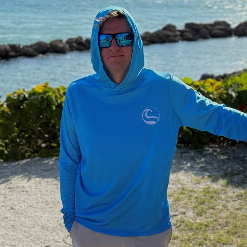 Man wearing the Blue Horizon Men's UV Hoodie with hood up, standing outdoors by the water
