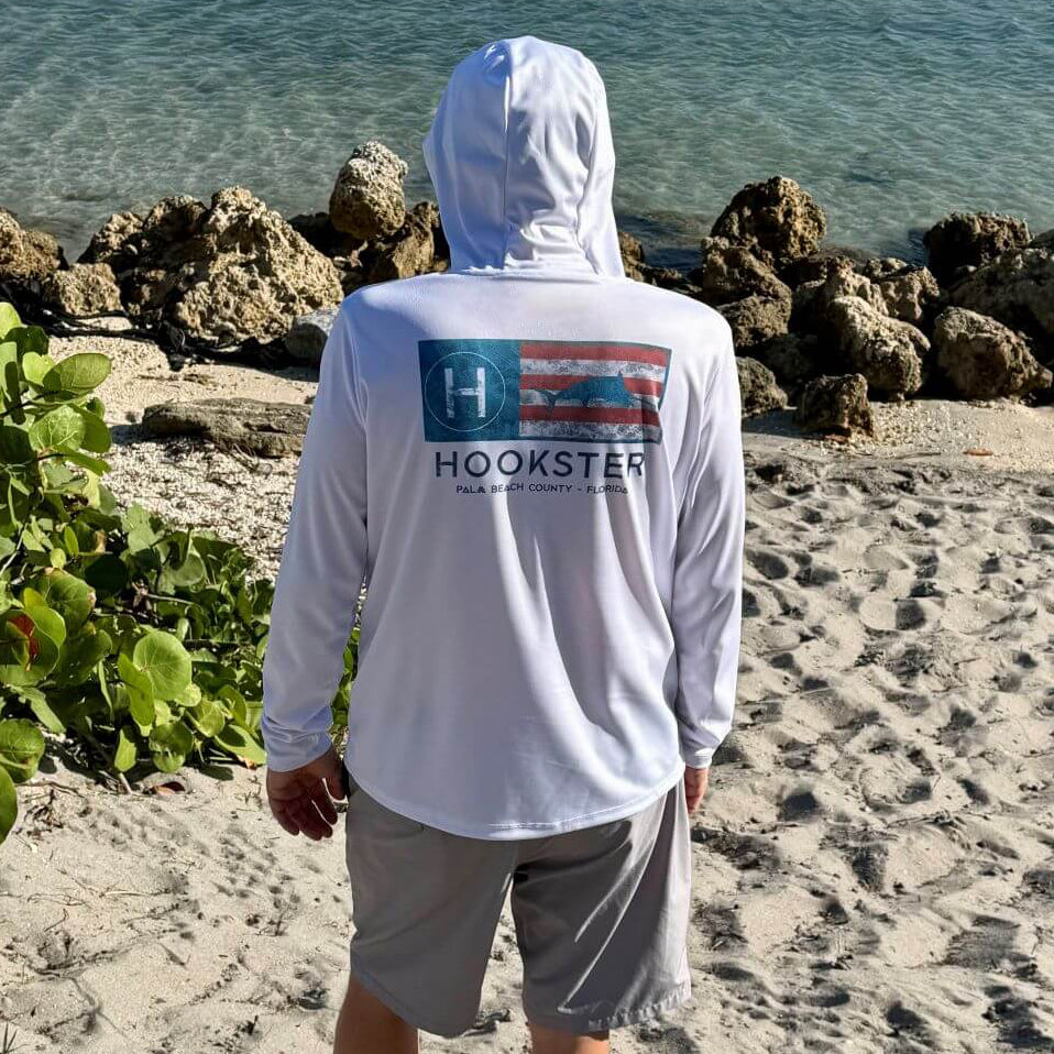 Back view of a man wearing the Coastal Flag Men's UV Hoodie in white with hood up, outdoors