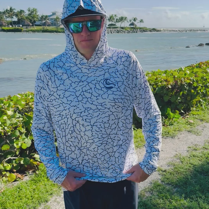 Video of an angler on the waterfront turning to show the front, back and thumbhole cuffs of the HOOKSTER Tide Trace UPF 50+ UV hoodie in white with a navy cracked-earth print