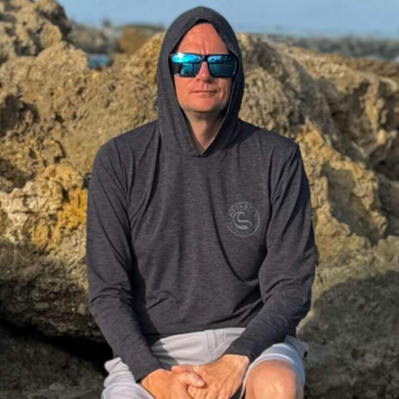 Man wearing the Reel Classic Men's UV Hoodie in charcoal gray, sitting outdoors
